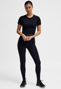 Sort ribbet crop top med korte ærmer parret med højtaljede sorte leggings. Har et tætsiddende design og subtilt mærke på livet.