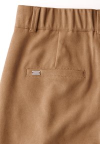 Vaaleat housut, joissa on teksturoitu kangas, varustettuna takataskulla, jossa on metallinen tarra, jossa lukee "STREET ONE STUDIO." Näkyvä elastinen vyötäröyksityiskohta.