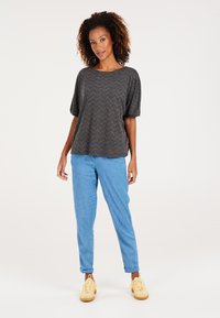 Grå overdimensioneret top med chevronmønster og korte ærmer, parret med lysblå tapered bukser og kridhvide snørebåndssneakers.