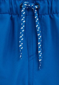 Material albastru cu șnur împletit albastru și alb trecut prin ochiuri negre, arătând cusături și textură detaliate.