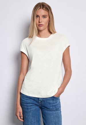 T-shirt bianco leggero con maniche corte arrotolate e scollatura rotonda, abbinato a jeans blu. Tessuto morbido, vestibilità casual.