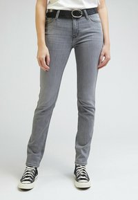Jeans en denim gris moulants, avec une ceinture noire à boucle argentée. Associés à des baskets montantes noires et blanches.