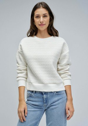 Weißer Sweatshirt mit Struktur und Zickzackmuster; gerippte Bündchen und Saum; kombiniert mit hellblauen Jeans. Sauberes, lässiges Design.