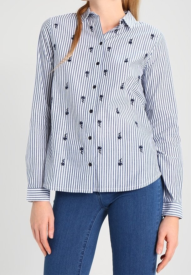 Chemise à rayures bleues et blanches avec boutons, ornée de broderies noires. Manches longues avec poignets boutonnés. Tissu doux et léger.