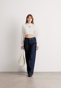 White ribbed crop sweater and dark blue loose jeans, paired with a beige bag. Simple design, no patterns, with a small logo on the sweater.
