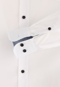 Weißes Hemd mit schwarzem Knopf, glatter Textur und kontrastierenden hellblauen Manschetten mit geometrischem Muster innen.
