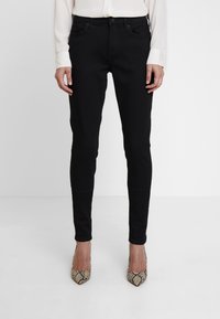 Black skinny jeans made of stretchy fabric, featuring a mid-rise waist, five-pocket design, and slim fit. Worn with python print heels.