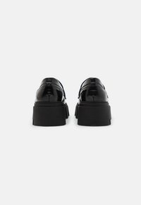 Scarpe in pelle verniciata nera con suola chunky, caratterizzate da una finitura liscia e un design minimalista. La vista posteriore evidenzia il dettaglio della suola a strati.