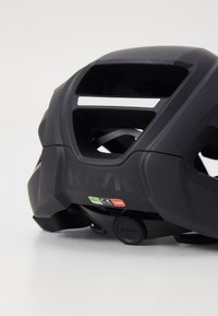 Casque KASK noir mat, avec de multiples aérations, une bande argentée, des sangles ajustables et des étiquettes de certification à l'arrière.