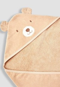 Bear-themed hooded towel in soft beige fabric, featuring a bear face with embroidered details and ear accents, with a textured terry underside.