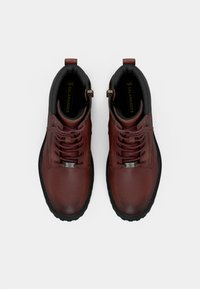 Par de botas de cano curto castanhas em pele com atacadores e solas pretas, vistas de cima sobre um fundo branco.