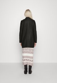 Mössa i ullblandning i mörkgrått, rak skärning med en ren bakseam. Kombinerad med en mönstrad kjol med ljusa och mörka ränder och svarta stövlar.