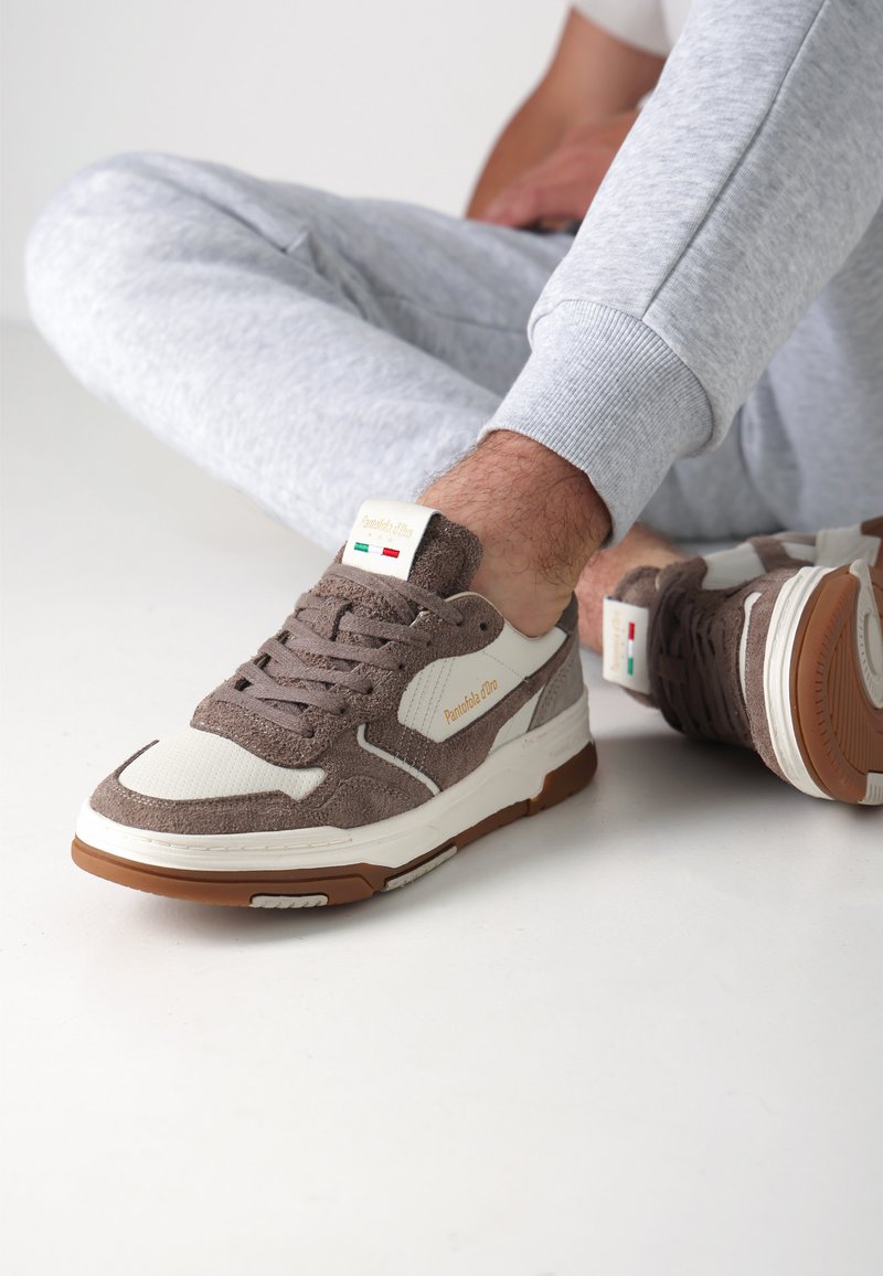 Brązowe zamszowe sneakersy z białymi skórzanymi akcentami i brązową gumową podeszwą. Posiadają przeszywane detale oraz metkę z logo na języku.