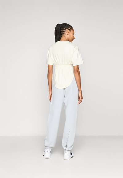 Light yellow short-sleeve top with an elasticized waist, paired with gray sweatpants and white athletic shoes. Simple and fitted design.