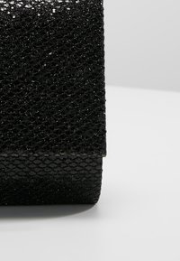 Pochette rectangulaire noire avec une surface texturée scintillante reposant sur un fond clair uni.