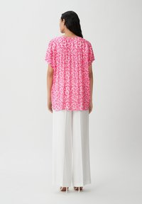 Blusa a maniche corte floreale rosa con un fit morbido, caratterizzata da un dettaglio arr gathered sul retro. Abbinata a pantaloni bianchi a gamba larga e tacchi alti.