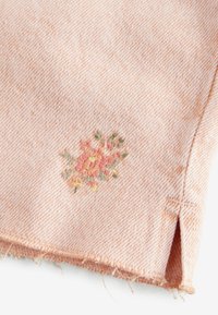 Tela de color melocotón con un tejido texturizado, presenta bordados florales en rosa y verde. Dobladillo sin coser con detalle de abertura lateral.