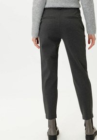 Harmaat kapenevat housut, joissa on sileä pinta, kahdella takataskulla ja vetoketjuyksityiskohdilla, yhdistettynä harmaisiin nilkkureihin.