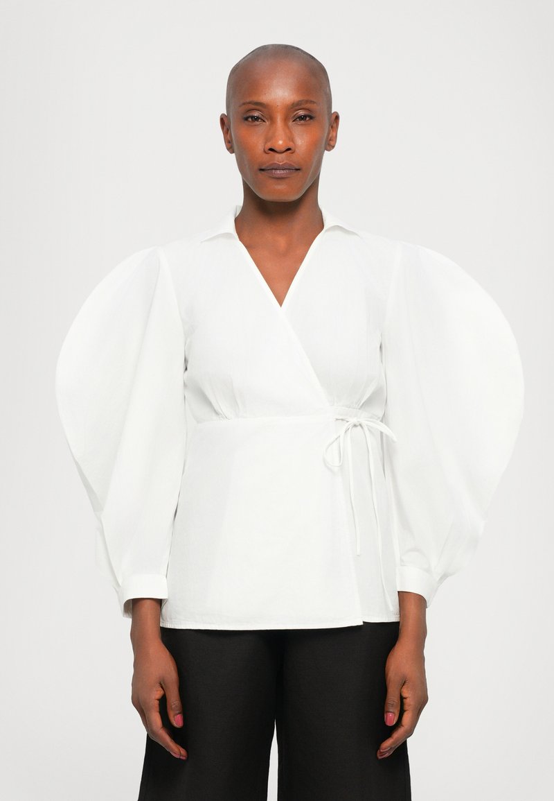 Witte blouse met een kraag, met volumineuze puffmouwen, gestrikt op de taille, gecombineerd met zwarte wijde broekspijpen. Glad stofoppervlak.