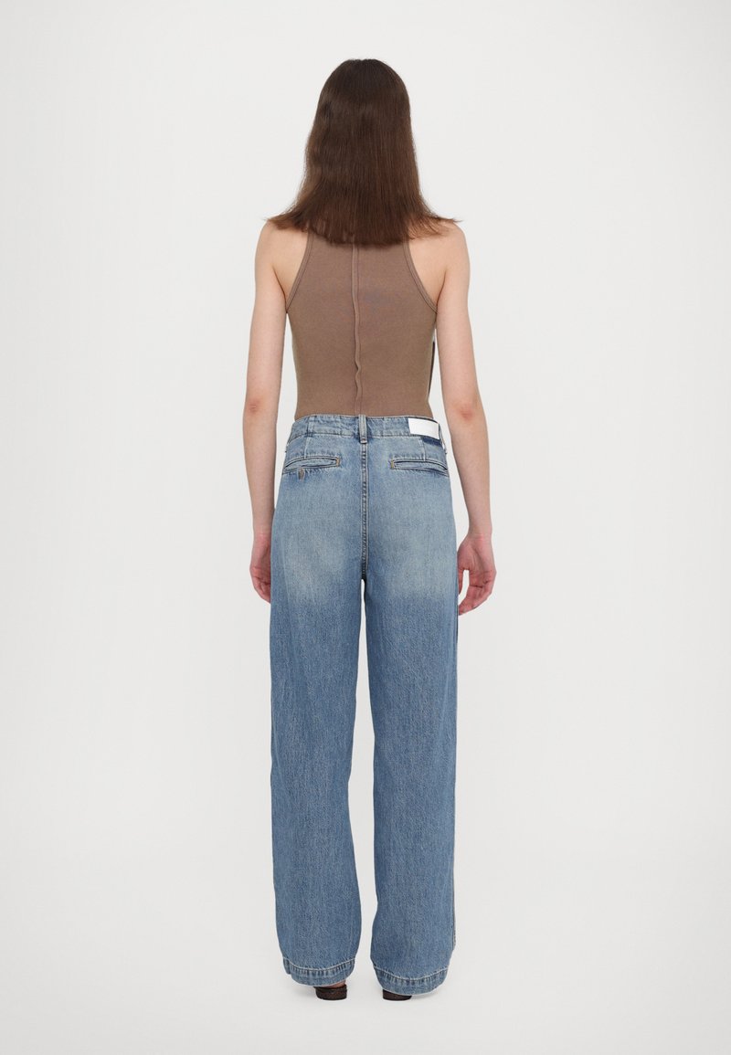 Braun gerippter Tanktop, kombiniert mit hochsitzen blauen, weit geschnittenen Jeans. Verfügt über zwei Gesäßtaschen und ein Etikett am Hüftbund.