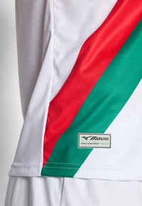 Hvit sportsskjorte med røde og grønne diagonale striper. Inkluderer en Mizuno-lapp som sier "Offisielt Lisensiert Produkt."