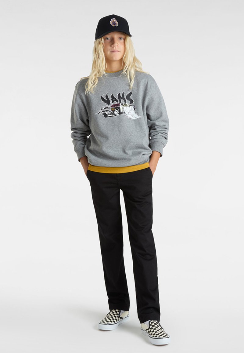 Grå sweatshirt med "VANS"-grafik, gul midja, svarta byxor och svarta och vita rutiga slip-on skor. En svart keps fulländar looken.