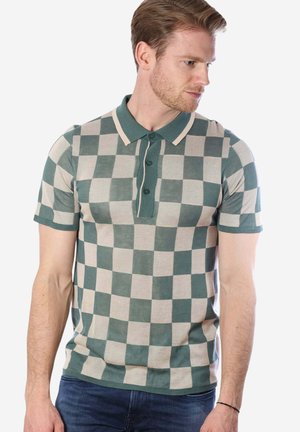 Mann trägt ein grün-beiges kariertes Kurzarm-Poloshirt und schaut zur Seite, Arme entspannt an den Seiten.