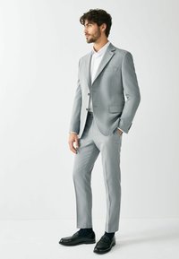 Light gray tailored suit with sleek fit, notch lapels, and single-button closure, paired with a white shirt and black loafers.