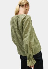 Groene bloes met borduursel in bloemenmotief, lange mouwen, geplooide halslijn en elastische manchetten. Geweven stof met bladeren en bloemenpatronen.