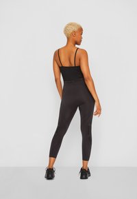 Top desportivo preto sem mangas com alças finas, combinado com leggings pretas ajustadas que apresentam detalhes texturizados e um logótipo ao longo da cintura.