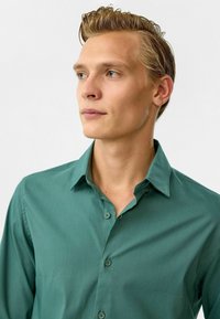 Groene button-up shirt met een gladde textuur, klassieke kraag en knopenlijst. Heeft kleinere knopen en een getailleerd ontwerp. Subtiele glans.