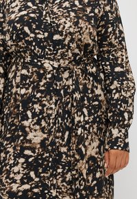 Robe à manches longues noire avec un motif abstrait beige et marron, dotée d'une taille cintrée avec une ceinture assortie et des poignets à boutons.