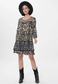 Schwarzes und cremefarbenes gemustertes Kleid mit langen, transparenten Ärmeln, gerüschtem Saum und einem Spitzen-Oberteil. Kombiniert mit schwarzen Cowboystiefeln und einem breitkrempigen Hut.