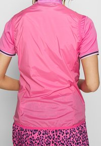 Růžové polo tričko s krátkým rukávem a lehkým, hladkým povrchem. Obsahuje vysoký límec a pruhované detaily na rukávech.