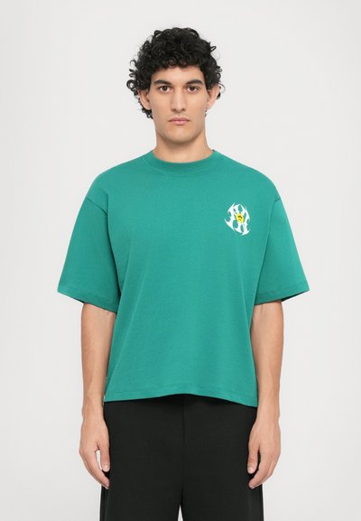 Green cotton t-shirt with short sleeves, round neckline, and a small, colorful graphic on the chest. Relaxed fit and soft texture.