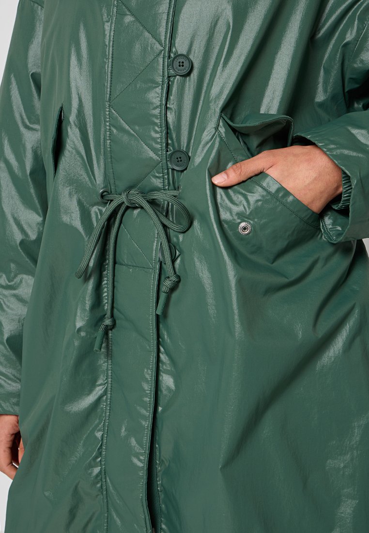 Chaqueta verde, brillante y a prueba de agua, con cintura ajustable, grandes botones y bolsillos laterales, que presenta un detalle de diseño acolchado.