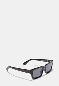 Mustat suorakulmaiset aurinkolasit tummilla linsseillä, muovikehys, hieman kaarevat varret, joissa on pieniä kultaisia yksityiskohtia edessä.