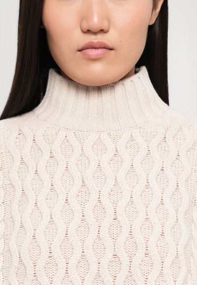 Light beige knitted sweater with a high collar, featuring a textured wave pattern and ribbed accents. Close-up view focuses on the neckline.