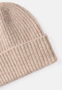 Gorro de malha canelada bege feito de lã macia; apresenta uma aba dobrada e pequenas manchas para textura e interesse visual.