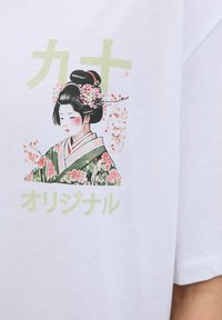 Bijela pamučna majica sa grafikom žene u cvjetnom kimonu, s zelenim japanskim tekstom iznad i ispod ilustracije.