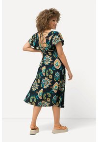 Schwarz mit Blumenmuster, Kleid mit kurzen, Rüschenärmeln, Schnürdetail am Rücken und fließendem, knielangem Saum. getragen mit beigen Plateausandalen.