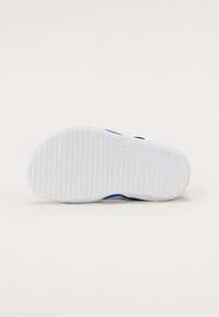 Nike-Schuhsohle, weißes Gummi mit strukturiertem Griffmuster, mit blauen Akzenten und einem Swoosh-Logo. Glatte Oberfläche, entworfen für Halt.
