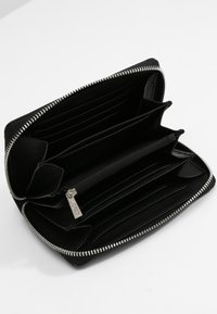 Cartera de cuero negro con cierre de cremallera, múltiples compartimentos para tarjetas, un bolsillo para monedas y un interior suave. Presenta detalles en metal de tono plateado.