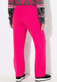 Fuksia vaaleanpunaiset verkkarit rennolla leikkauksella, pehmeällä pinnalla ja joustavalla vyötäröllä, yhdistettynä mustiin ja valkoisiin urheilukenkien kanssa.