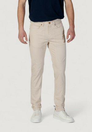 Pantaloni slim-fit beige con tasche frontali, chiusura con bottone e dettagli di cucitura discreti. Indossati con sneakers bianche e una maglia blu navy.