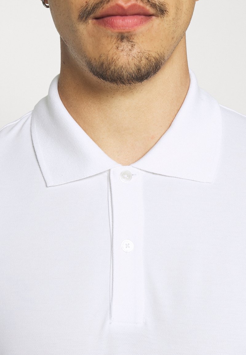 Vit polo skjorta med en texturerad tyg, med klassisk krage, tre-knapps knäppning och en ren, enkel design.