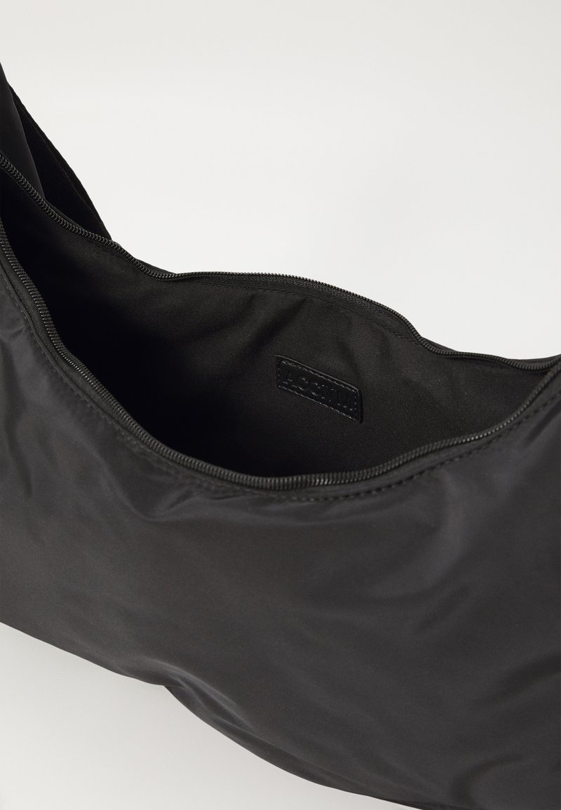 Sac en nylon noir avec une texture lisse, conçu avec une fermeture éclair sur le dessus et une étiquette à l'intérieur, montrant un style simple et fonctionnel.