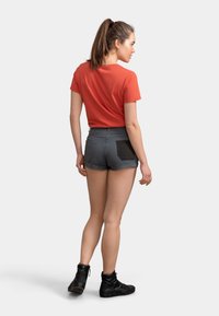 Chemise rouge à manches courtes accompagnée d'un short en denim gris avec des poches arrière noires. Le modèle porte des bottines noires à la cheville. Fond neutre.