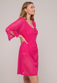 Mesh dek jurk in helder roze, met een diepe V-hals, driekwart mouwen en een vetersluiting bij de halslijn.