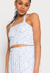 Top cropped de estampado floral azul claro com alças halter, apresentando um decote em quadrado e um tecido texturizado. Design solto.